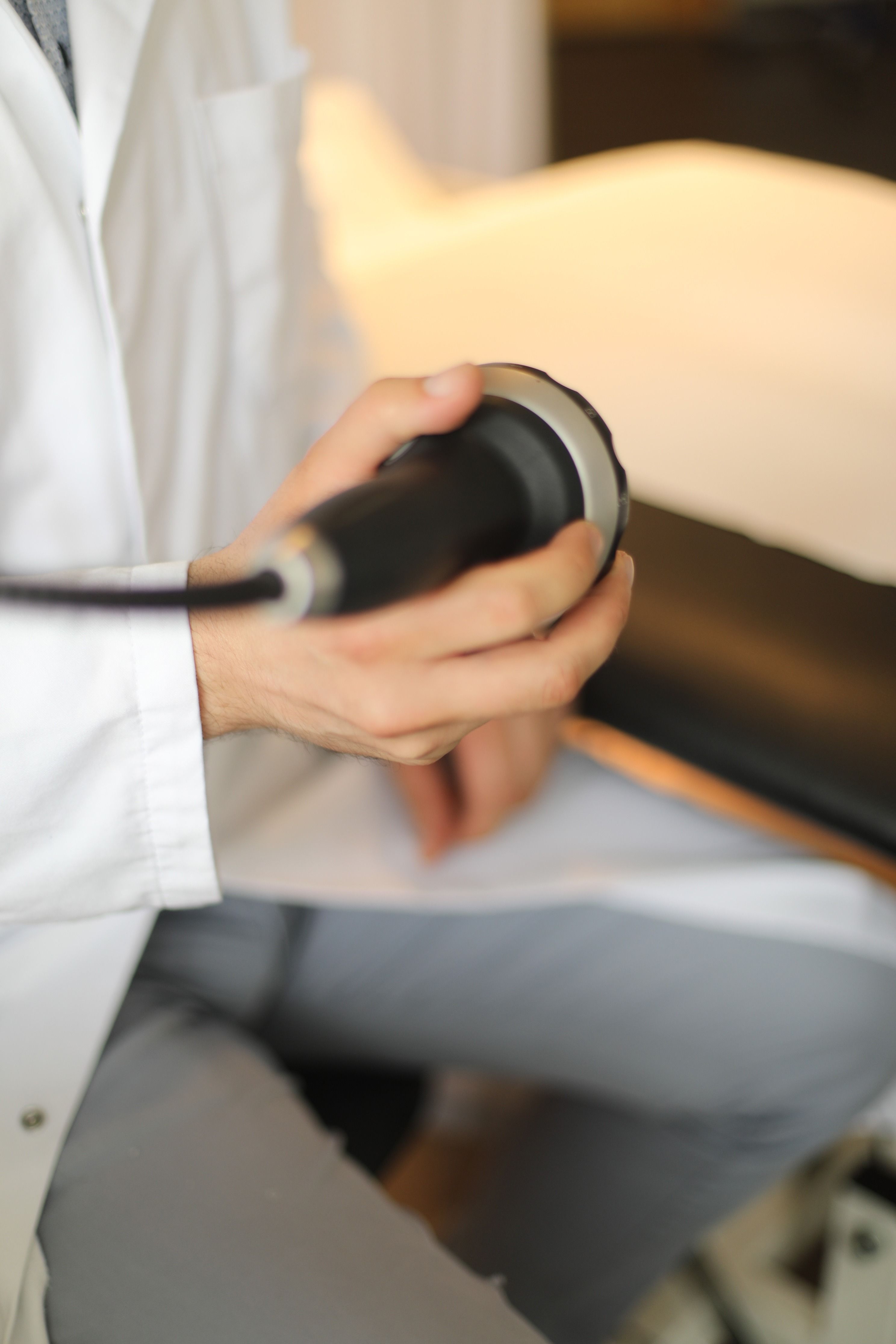 Arzt hält das Handstück eines Stoßwellentherapie-Geräts vor der ESWT-Behandlung